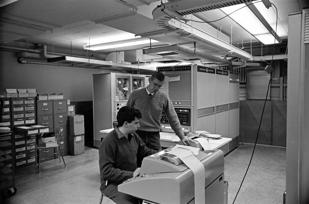 Dr. Kurtz, standing, worked with a student, Michael Busch, to test a new computer in the basement of College Hall at Dartmouth in 1964.Credit...Adrian N. Bouchard/Rauner Special Collections Library at Dartmouth